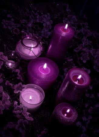 A lot of magic purple and velvet violet colors candles burn on the blue background with flowers.の写真素材