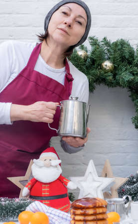 Middle aged lady chef on the white kitchen with cup of tea or coffee on the New Year background.の写真素材