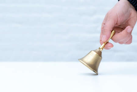 Hand holds a golden bell on the white background, copy space, concept school, teather or manager in hotel.の写真素材