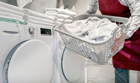 Worker in the hotel holds a lot of towels in hands near Dry machine in the laundry.の写真素材