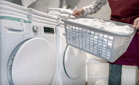 Worker in the hotel holds a lot of towels in hands near Dry machine in the laundry.の写真素材
