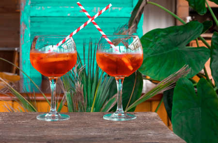 Aperol spritz cocktail in glass on the old wooden table on the green background with tropical leaves.の写真素材