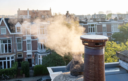 Smoke from chimney pipes at the rooftop of ordinary family houses in the Netherlands, sunrise on the roof of the city center.の写真素材