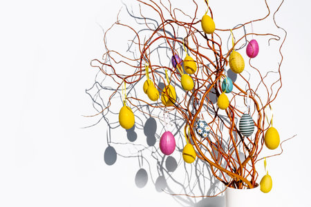 Thin spring branches with yellow and pink eggs on a white background with a bright sun as a symbol of the Easter holiday in Europe, Netherlandsの写真素材