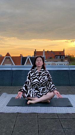 Middle-aged woman doing morning exercises on her rooftop against the backdrop of dawn and old Dutch housesの写真素材