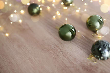 Green Christmas tree balls on a light wooden background. garland defocused lights. Preparation for the New Year. Christmas background with copy space.の写真素材