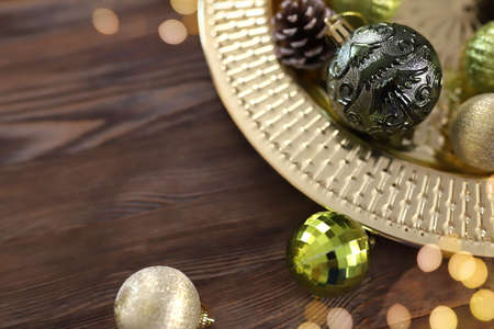 Close-up golden round tray with green and gold Christmas tree balls and pine cones on wooden background. Christmas background with copy space. Gerland defocused lights. Preparation for the New Year.の写真素材