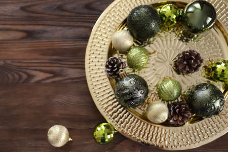 Golden round tray with Green and gold Christmas tree balls and pine cones on wooden background. Christmas background with copy space. Preparation for the New Year. High quality photoの写真素材