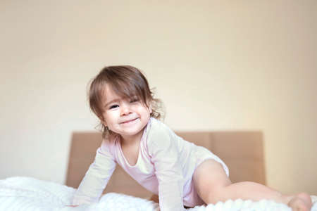 Happy child girl having fun jumps and plays big parents bed. Child with tousled hair is having fun on a beige bed. High quality photoの写真素材