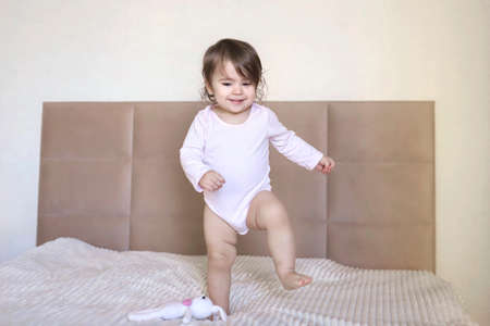 Happy child girl having fun jumps and plays big parents bed with teddy bear. High quality photo
