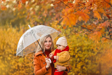 young girl with a baby in her arms under an umbrella in the park in autumnの写真素材