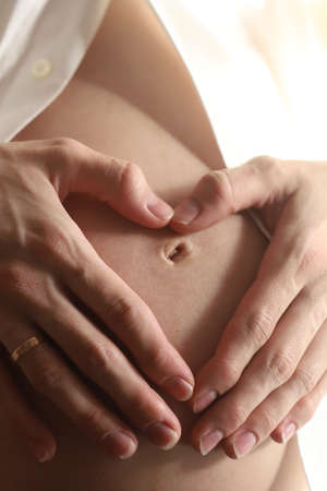 Close up of a pregnant woman forming a heart on her belly with her hands. Happy young mother...