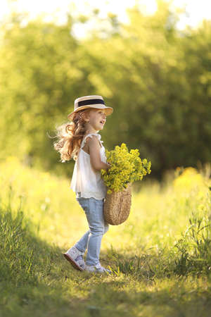 Little girl runs around the field with flowers in a straw hat. Child is having fun on the street. Concept of healthy child without allergies. High quality photoの写真素材