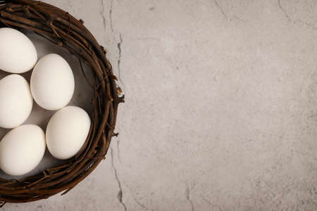 White chicken eggs in a nest on gray stone background. Top view. Free space. Easter eggs. High...