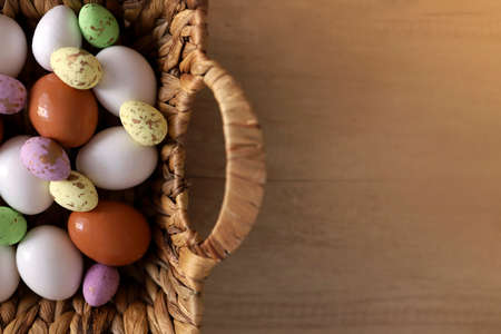 chicken eggs lie with a straw basket on wooden background.. Top view. Free space. Easter eggs. High...