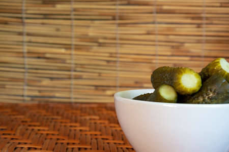 Pickles in a small deep plate of white color on a wooden table of vines and against a background of reeds. Free space.の写真素材