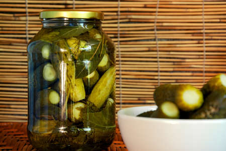 Pickled cucumbers in a jar of spices and a small white bowl with pickled cucumbers in the...