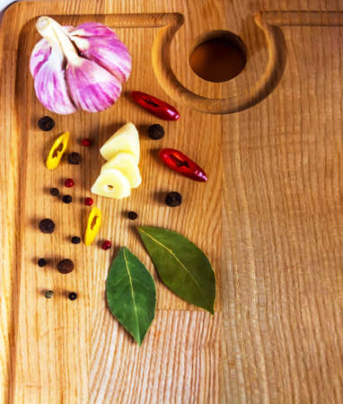A whole head and a clove of garlic, cut into slices, hot red and yellow peppers, cut into rings, a bay leaf and a mixture of peas are on a wooden cutting board.の写真素材