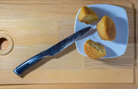 Freshly baked muffins cut with a knife on a square plate on a wooden backgroundの写真素材