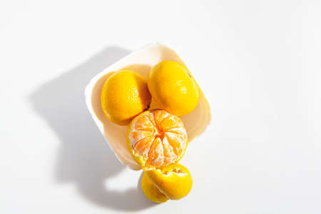Two whole tangerines and one half peeled in a square white bowl against a white background. Isolate....