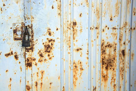 Old metal gate covered with rust with a new black lock.の写真素材