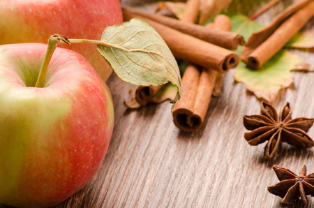 Red apple with green leaves, cinnamon and anise on a tableの写真素材