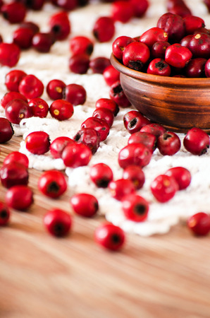 Hawthorn berries in a clay bowl and scattered on the tableの写真素材