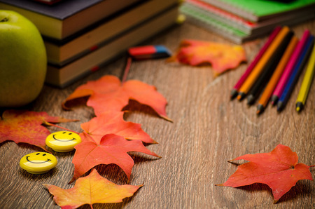 Books, notebooks, pencils,eraser, Apple and autumn leaves on the table