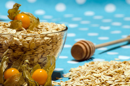 Oat flakes scattered on the table and in the bowl, the cherry and spoon for honey