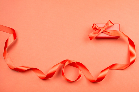 Red gift box with a ribbon on red background. Flat lay, holiday concept.の写真素材