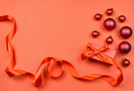 Gift box with a ribbon and red Christmas balls on red background. Christmas background. Flat lay.の写真素材
