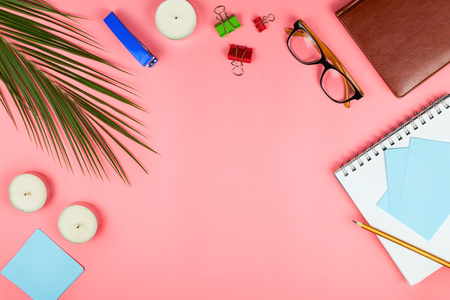 Business flatlay with glasses, palm leaf, candles, stapler, pen, notebook, colorful clipper and paper notes. Concept of a woman's work place. Flat lay. Pink background. Copyspaceの写真素材