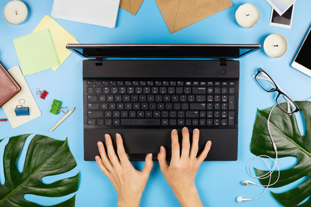 Beautiful flatlay with woman's hands printing, a laptop, mobile phone, glasses, philodendron leaves and other business accessories. Concept of a home office. Flat lay. Blue background.の写真素材