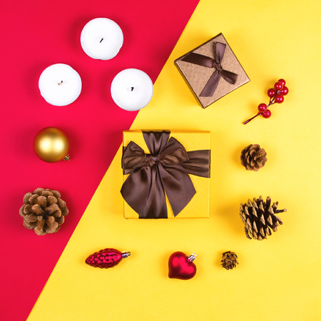 Colorful flatlay with various Christmas items, decor and gifts, including gift boxes, candles, pine cones etc. Red and yellow background. Christmas concept, squareの写真素材