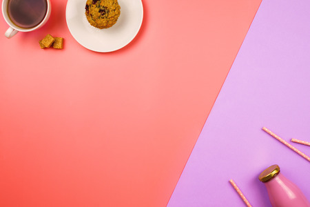 Flatlay with a blueberry muffin and cup of tea on one side and bottle of juice or smoothie with straws on the opposite side. Healthy and/or unhealthy breakfast concept. Pink and violet background.の写真素材