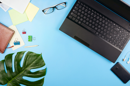 Beautiful flatlay with a laptop, glasses, philodendron leaves and other business accessories. Concept of a home office. Flat lay. Blue background.の写真素材