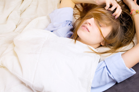 Young girl lying in her bed with messy hair covering her face. Selective focus, morning or night sleep concept.の写真素材