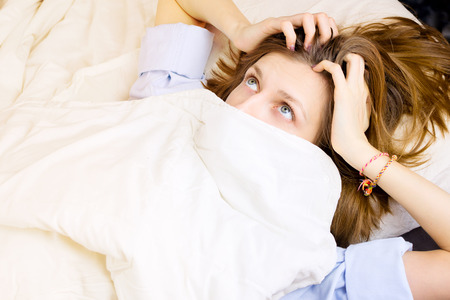 Young girl lying in her bed, face covered by blanket with eyes wide open with surprise. Selective focus, morning or night sleep concept.の写真素材