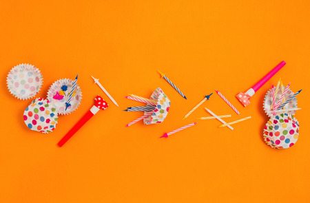 Flatlay with various party accessories: horns, candles, cupcake liners etc. Orange background.の写真素材