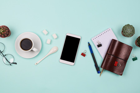 Business flatlay with smartphone with black copyspace screen, cup of coffee, succulents and cactuses and other business accessories. Mint color background. Top viewの写真素材
