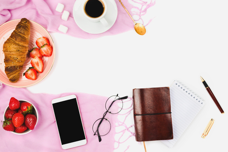Beautiful flatlay arrangement with wholewheat croissant, cup of espresso coffee, fresh strawberries and business accessories: concept of busy morning or breakfast, white background. Copyspaceの写真素材