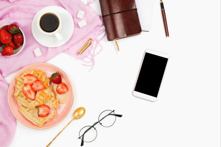 Beautiful flatlay arrangement with cup of coffee, hot waffles with cream, smartphone with black copyspace and other business accessories: concept of busy morning breakfast, white background.の写真素材