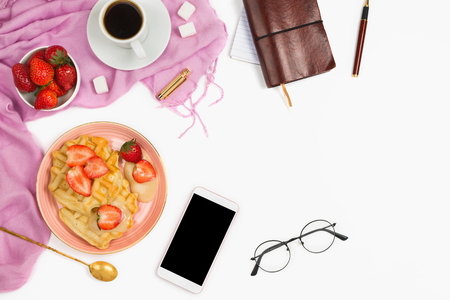 Beautiful flatlay arrangement with cup of coffee, hot waffles with cream and strawberries, glasses and other business accessories: concept of busy morning breakfast, white background.の写真素材