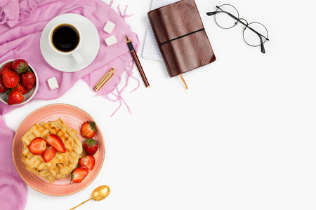 Beautiful flatlay arrangement with cup of coffee, hot waffles with cream and strawberries, glasses and other business accessories: concept of busy morning breakfast, white background.の写真素材