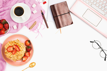 Beautiful flatlay arrangement with cup of coffee, hot waffles with cream and strawberries, laptop and other business accessories: concept of busy morning breakfast, white background.の写真素材