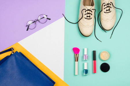 Stylish flatlay with female fashion accessories and clothes: white shoes, blue bag, glasses and cosmetics, blue, violet, white and yellow background. Copyspaceの写真素材