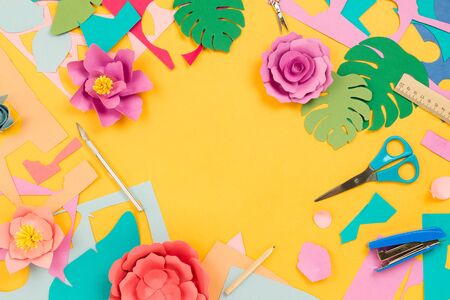 Various stationary supplies, colored paper, papercraft flowers on yellow background. Concept of creativity or art, flatlayの写真素材