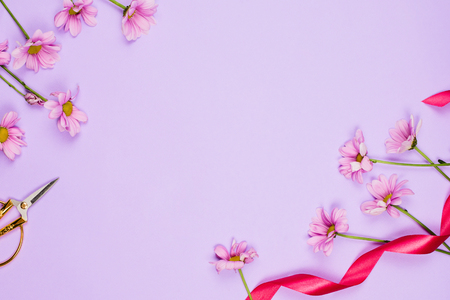 Flatlay frame arrangement with violet daises, scissors and ribbon, violet background, copyspaceの写真素材