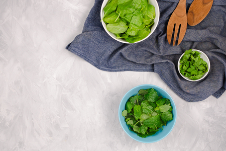 Fresh greens for a salad on cement background: spinach, mint and parsley on dark blue towel with wooden spoons, copyspaceの写真素材