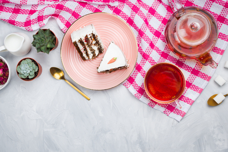 Vegan carrot cake pieces with glass teapot and cup of tea, spoons, dried rose buds and sugar cubes, tea time concept, flatlay, cement backgroundの写真素材